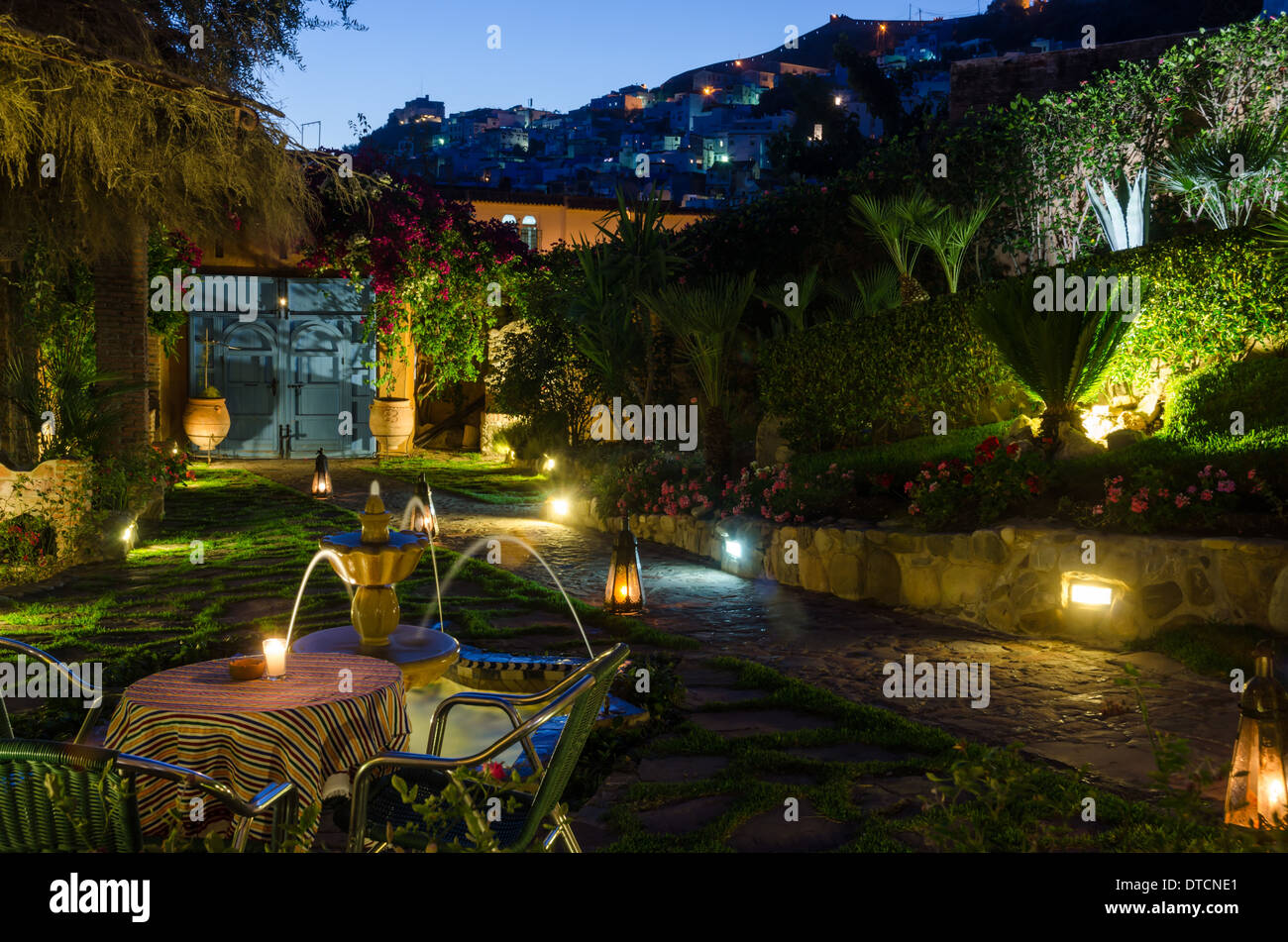 Ein marokkanische eingezäunten Garten ist herzlich bei Einbruch der Dunkelheit beleuchtet, wie Lichter in den Fenstern des nahe gelegenen Hang Häuser erscheinen. Stockfoto