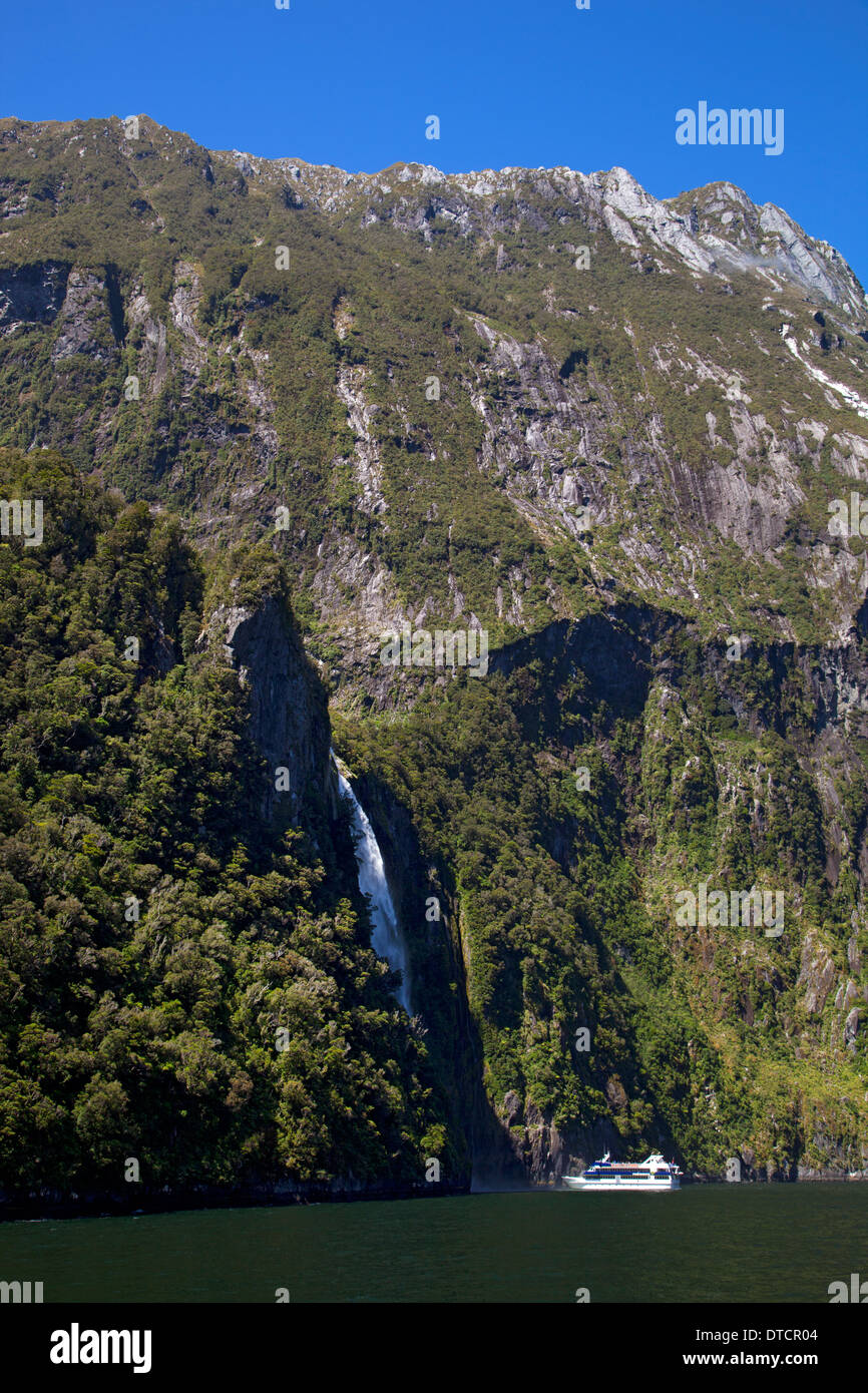 Touristenboot neben Wasserfall am Milford Sound, Fiordland, Südinsel, Neuseeland Stockfoto