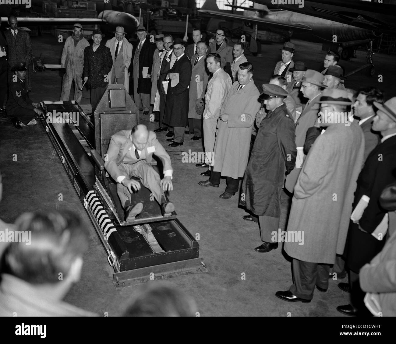 US-Armee Fliegerarzt Oberstleutnant John Paul Stapp (rechts) zeigt den Gee-Whiz Rakete Schlitten für eine Gruppe von Honoratioren mit Howard Hasbrook als Demonstrator 17. April 1956 auf der Edwards Air Force Base, CA in der Maschine zu sitzen. Stockfoto