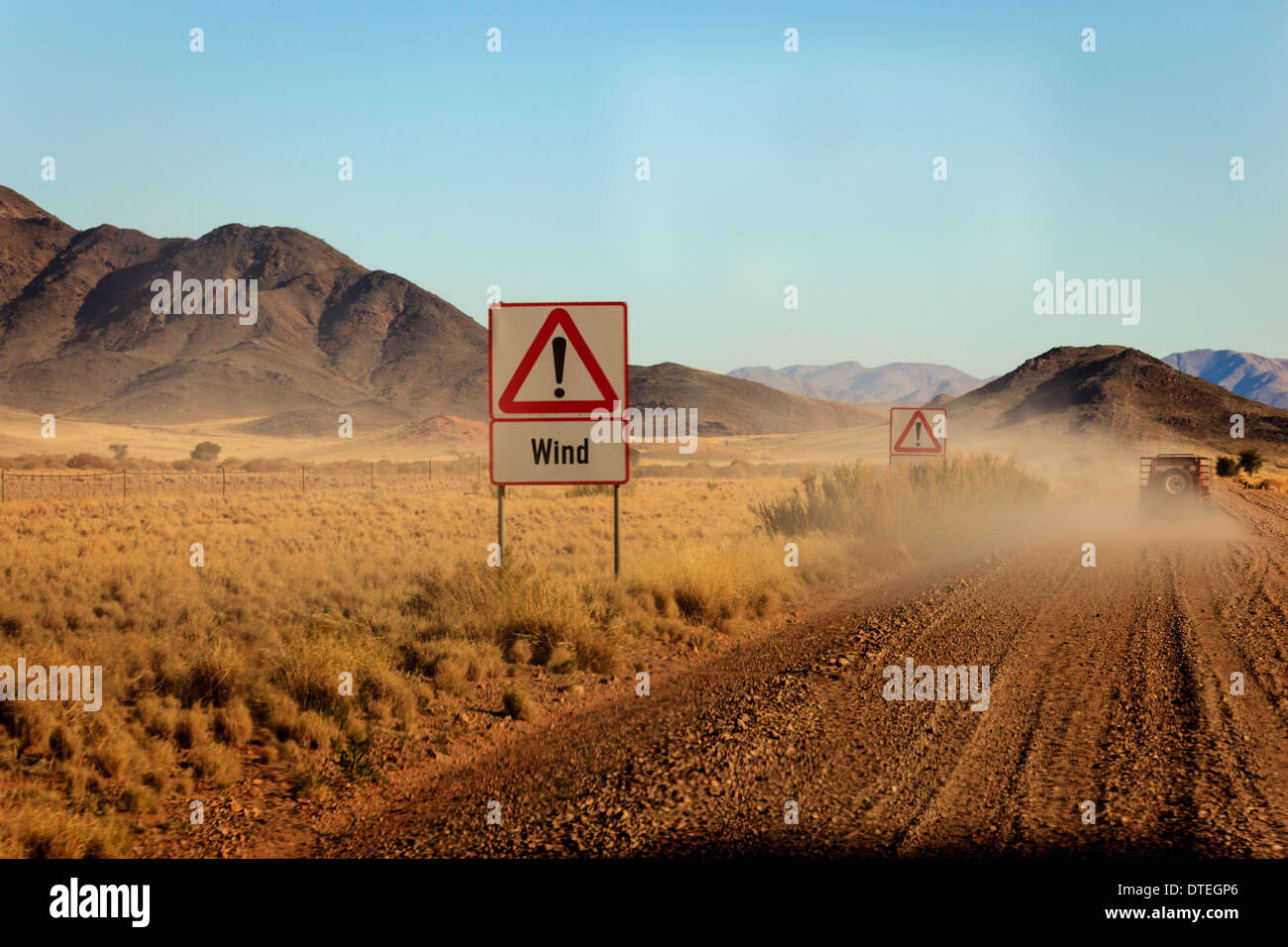 Lange Strecke der unbefestigten Autobahn mit Straßenschildern für Wind durch die namibische Wüste, die sich den Bergen in Afrika nähert. Stockfoto