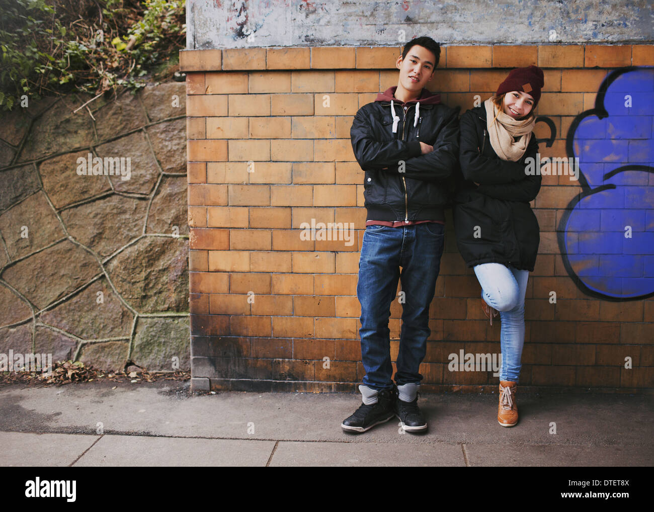 Schöner junger Mann und Frau in warme Kleidung zusammen stützte sich auf eine Wand im Freien stehen. Asiatische Teenager-Paar posieren Stockfoto