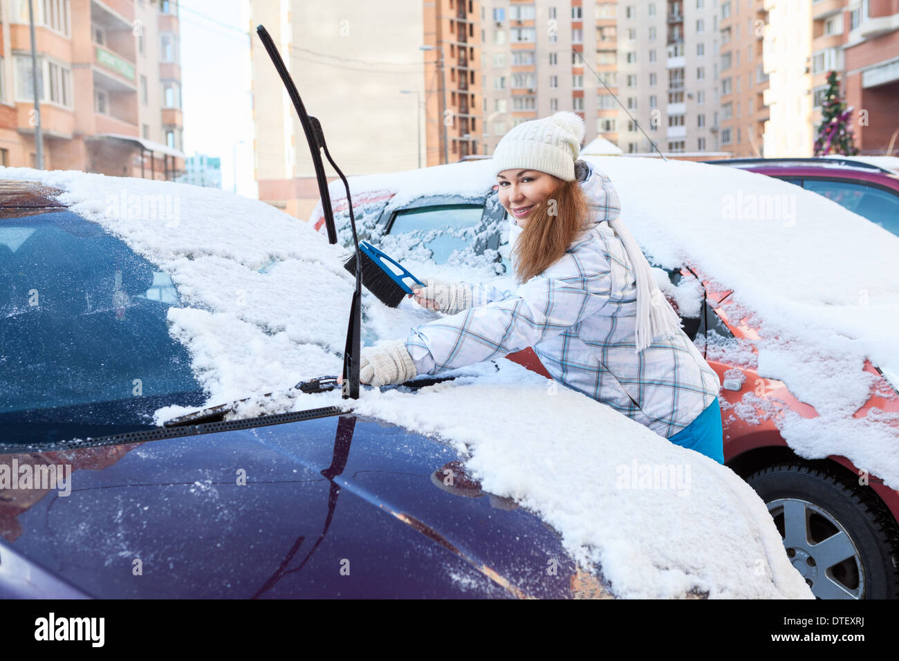 Parkplatz - junge Frau entfernen Schnee vom eigenen Auto mit Pinsel Stockfoto
