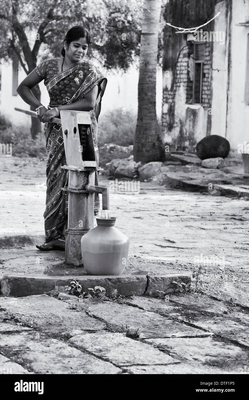 Indische Frau Füllung Kunststoff Wassertopf aus einem ländlichen Dorf Handpumpe. Andhra Pradesh, Indien. Monochrom Stockfoto