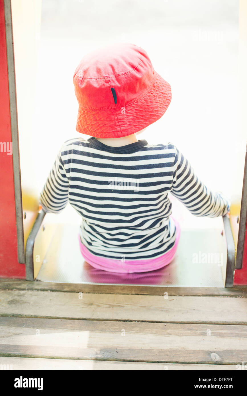 Kindheit-Lifestyle-Moment. Kleines Mädchen im Lesen Sie Hut sitzt an der Spitze einer Folie in einen Spielplatz für Kinder. Stockfoto