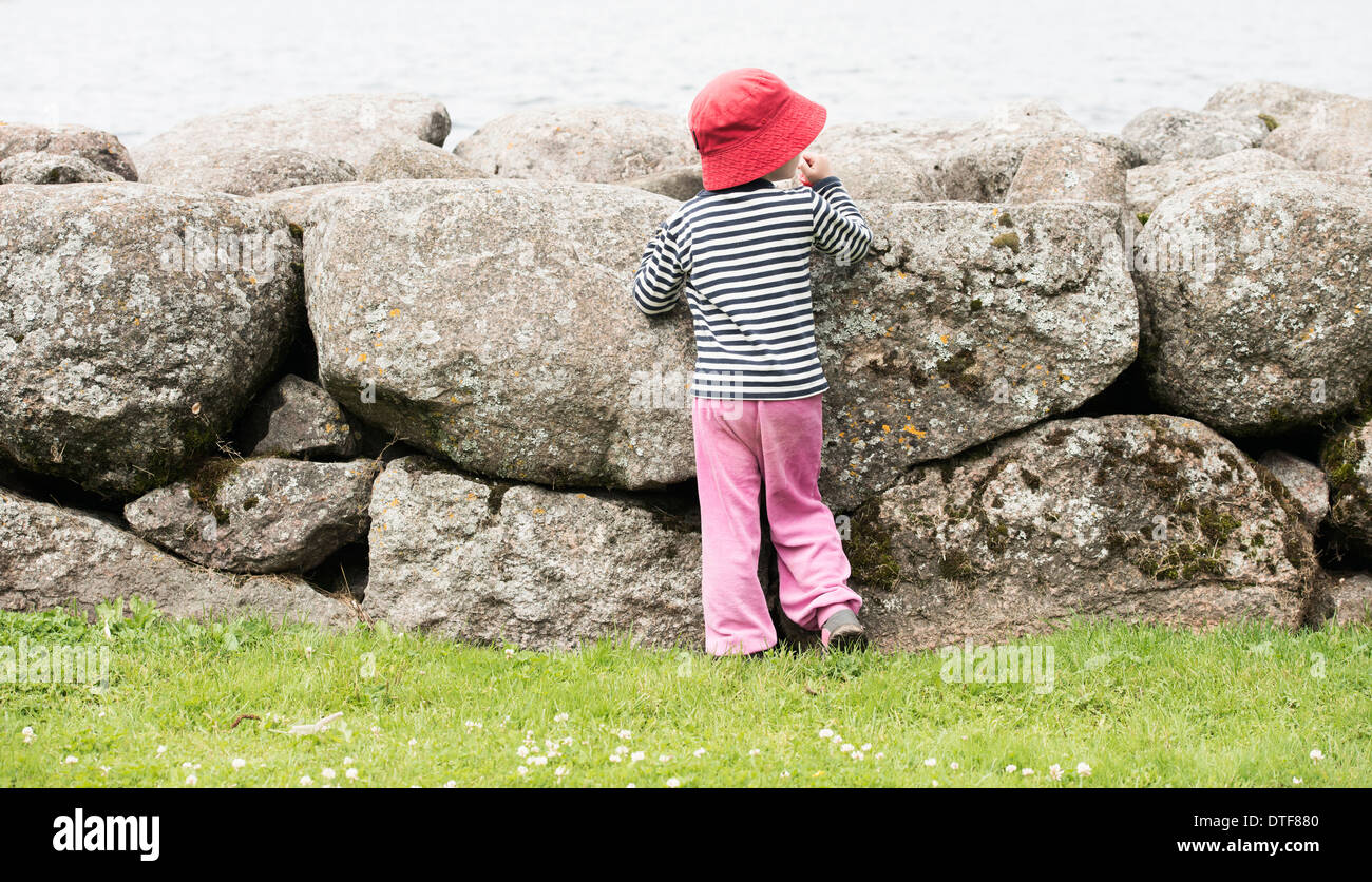 Kleines Mädchen allein von großen Steinen, die das Meer zu beobachten Stockfoto