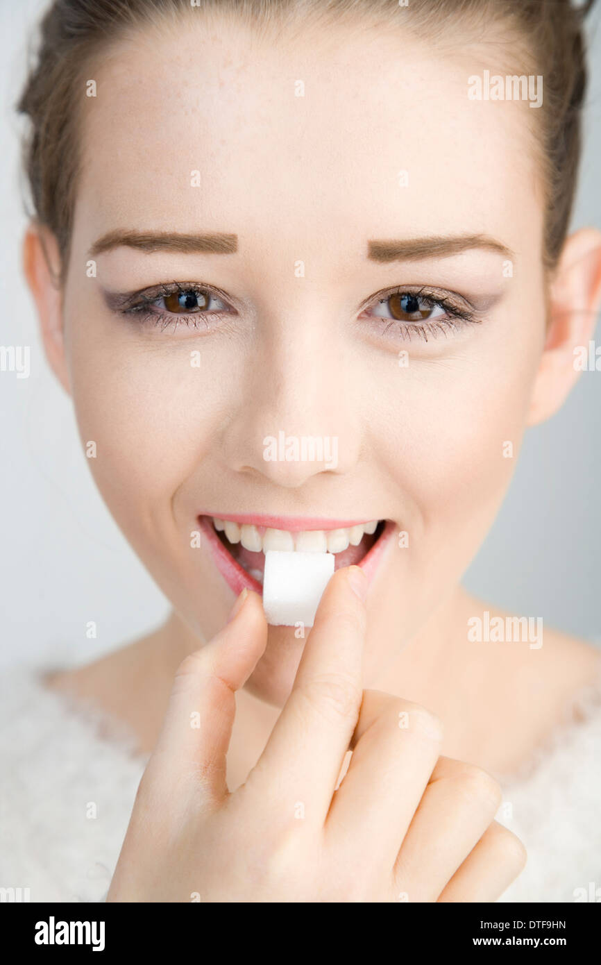 Ein ziemlich junges Mädchen hält ein Stück Würfelzucker auf den Mund. Stockfoto