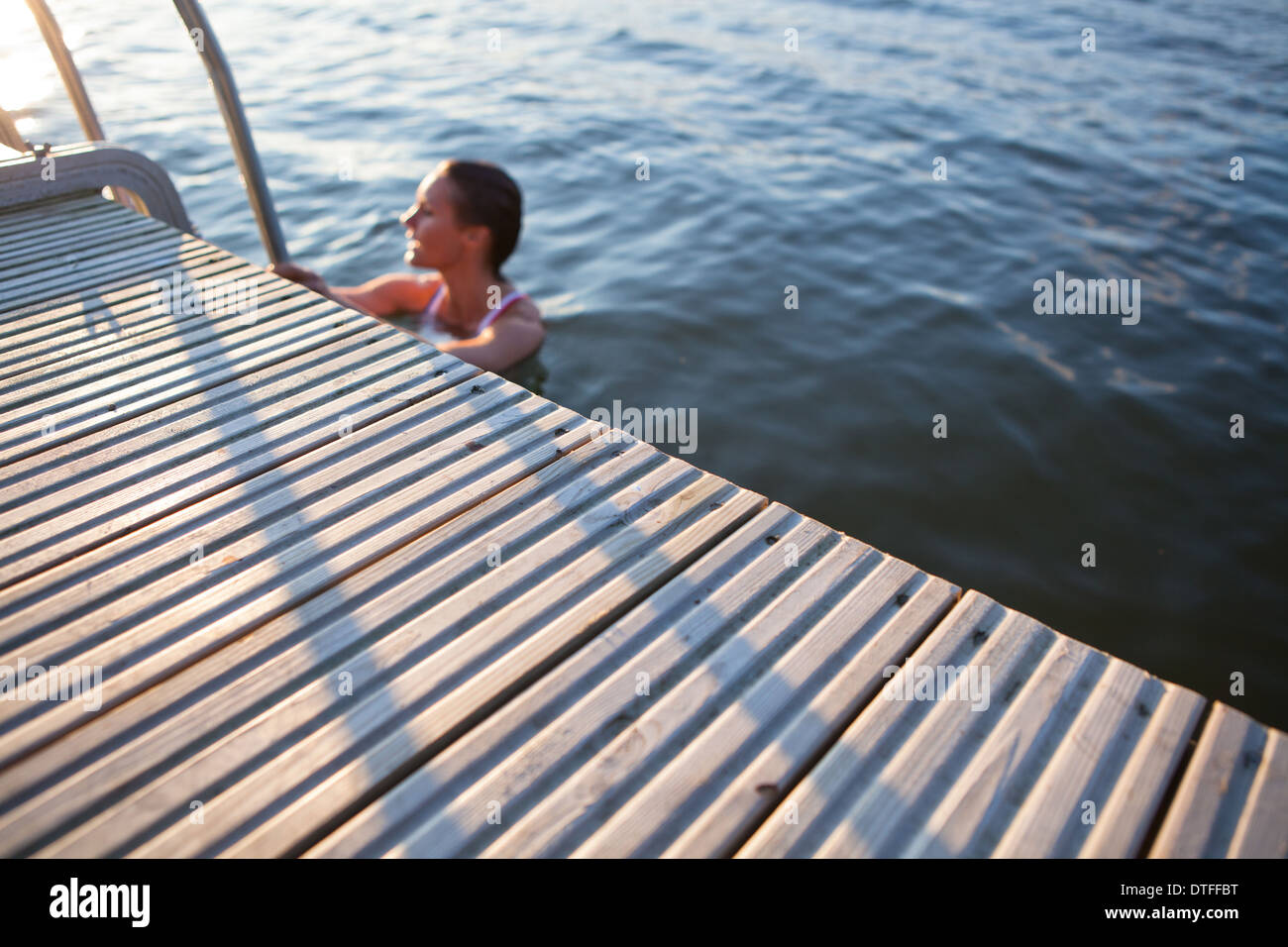 Rand der Holzsteg im Fokus mit Frau im Wasser festhalten an Leiter Stockfoto