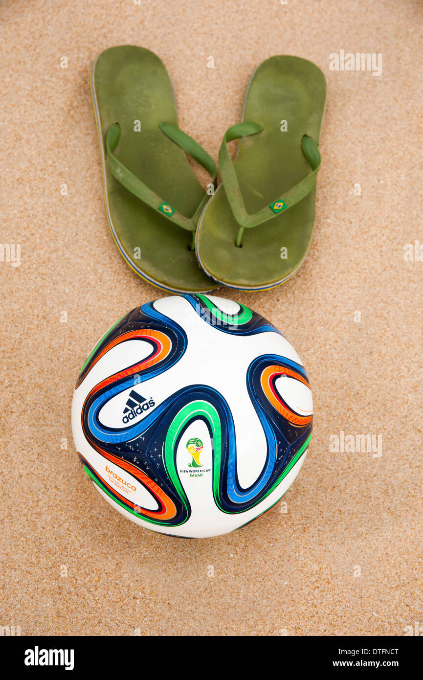 Brazuca (Nachbau), offiziellen Spielball für die FIFA WM 2014 in Brasilien in den Sand neben abgenutzten grünen flip-flops Stockfoto
