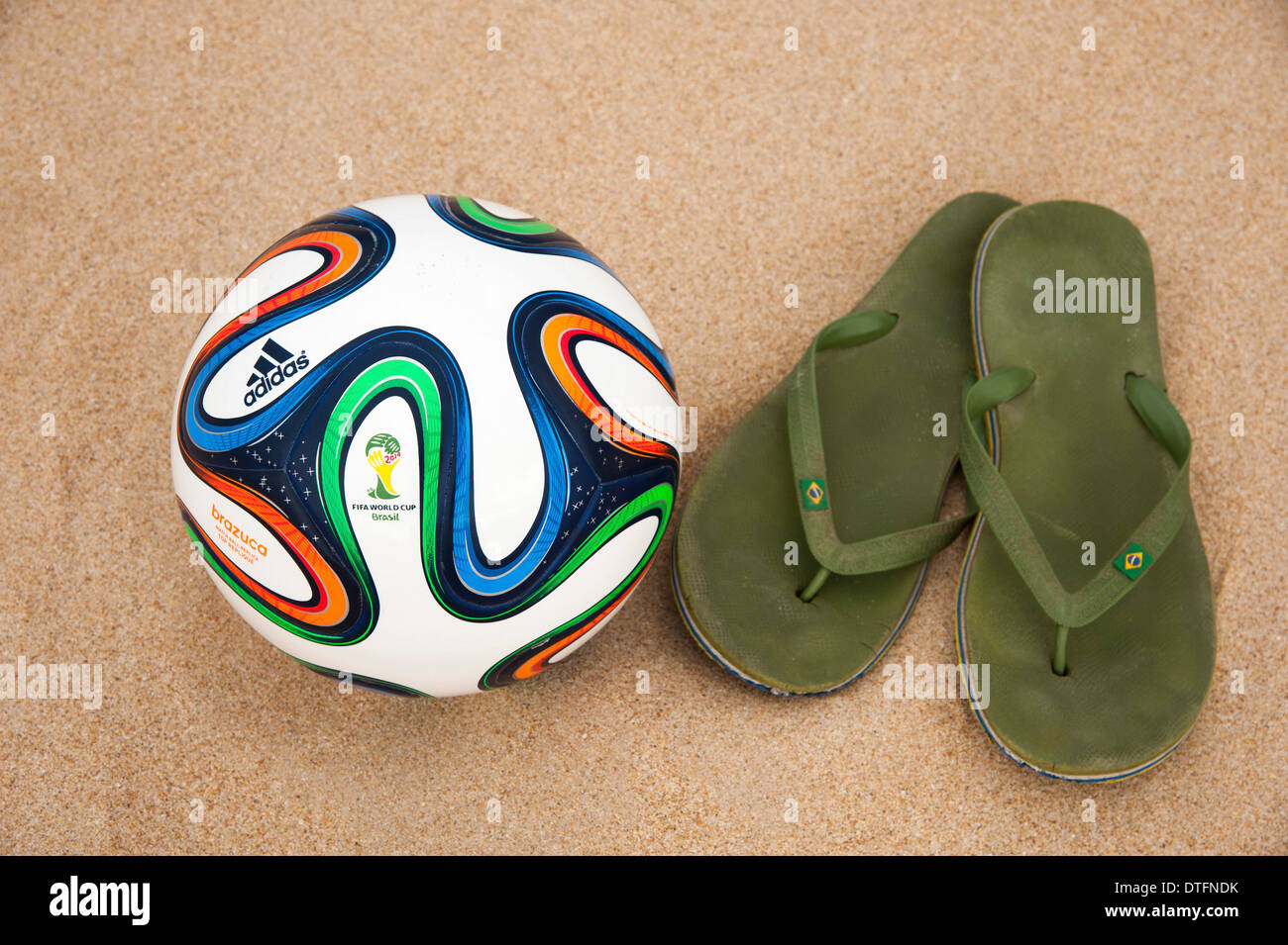 Brazuca (Nachbau), offiziellen Spielball für die FIFA WM 2014 in Brasilien in den Sand neben abgenutzten grünen flip-flops Stockfoto