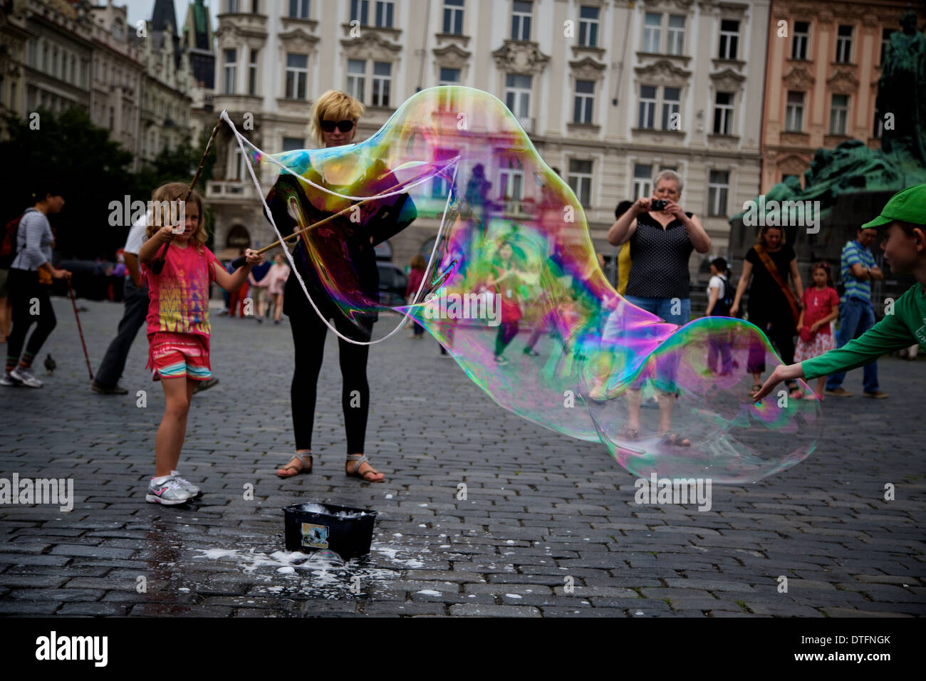 Ein junges Mädchen bläst eine große Seifenblase Stadtplatz als es von einem anderen Kind zu platzen. Stockfoto