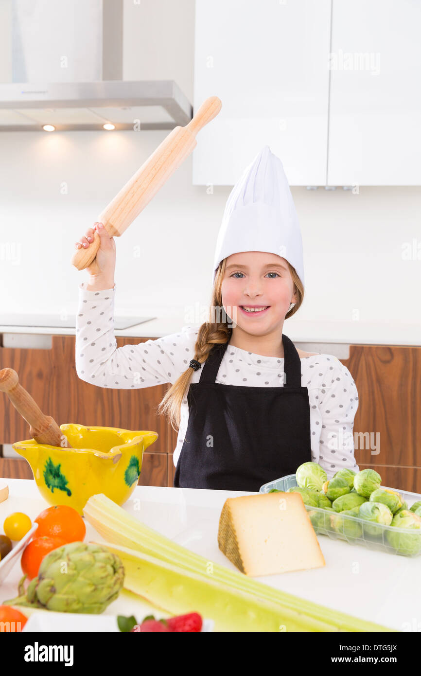 Blonde junge Mädchen Juniorchef auf Arbeitsplatte lustige Geste mit Walze kneten Stockfoto