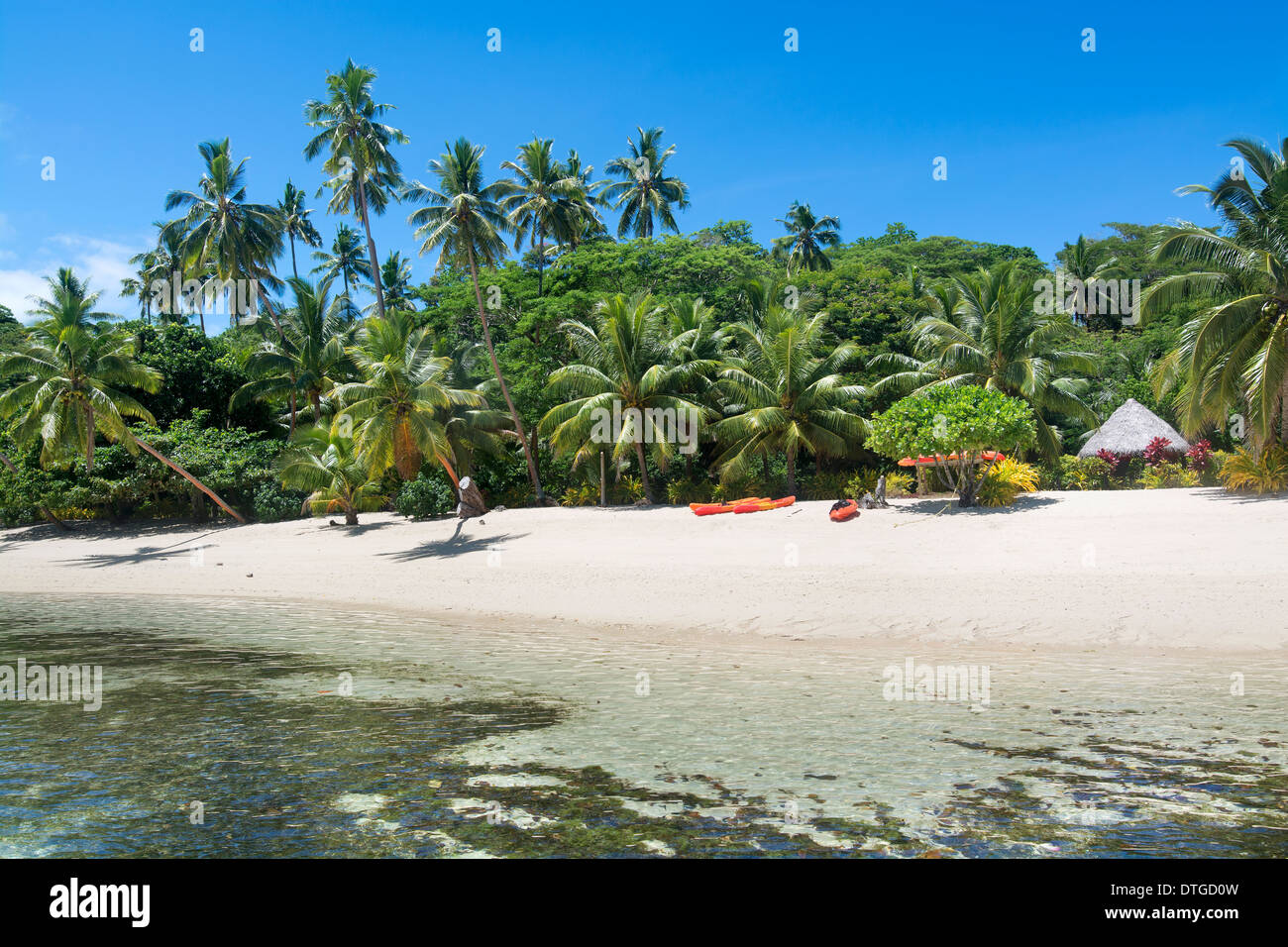 Ein Blick auf einem fidschianischen tropischen Resort aus dem Wasser, seine üppige Umgebung und Freizeit-Kajaks am Strand Stockfoto