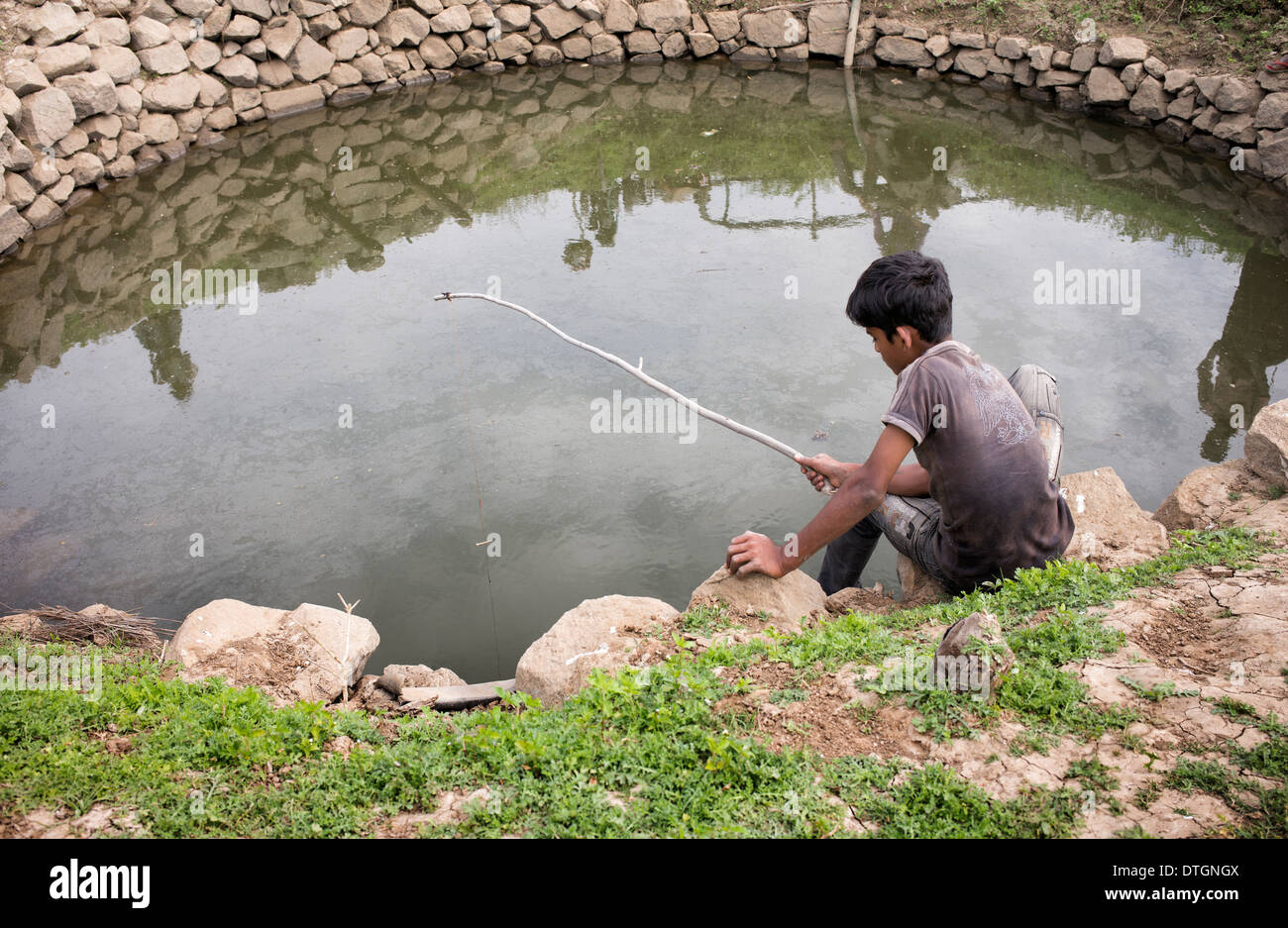 Indischer Junge mit hausgemachten Ruten in einem Brunnen in der indischen Landschaft Angeln.  Andhra Pradesh, Indien Stockfoto
