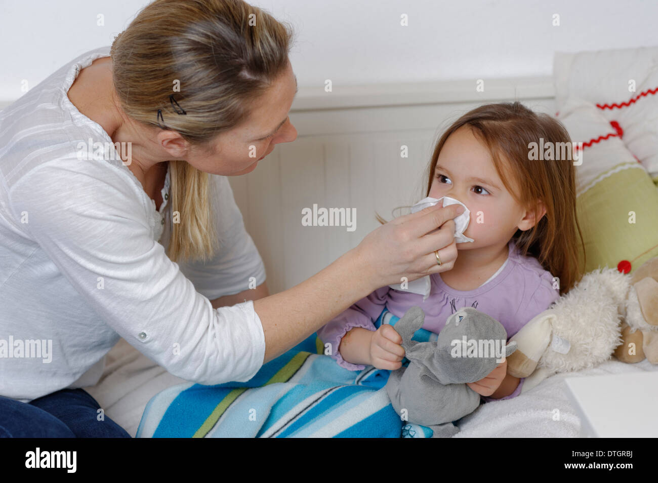 Mutter kümmert sich um ihre kranke Tochter, Abwischen des Mädchens Nase, Mädchen im Bett liegend Stockfoto