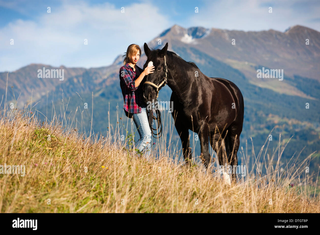 Eine junge Frau und ein schwarzes Hannoveraner Pferd stehend auf einer Bergwiese im Herbst, Nord-Tirol, Österreich Stockfoto