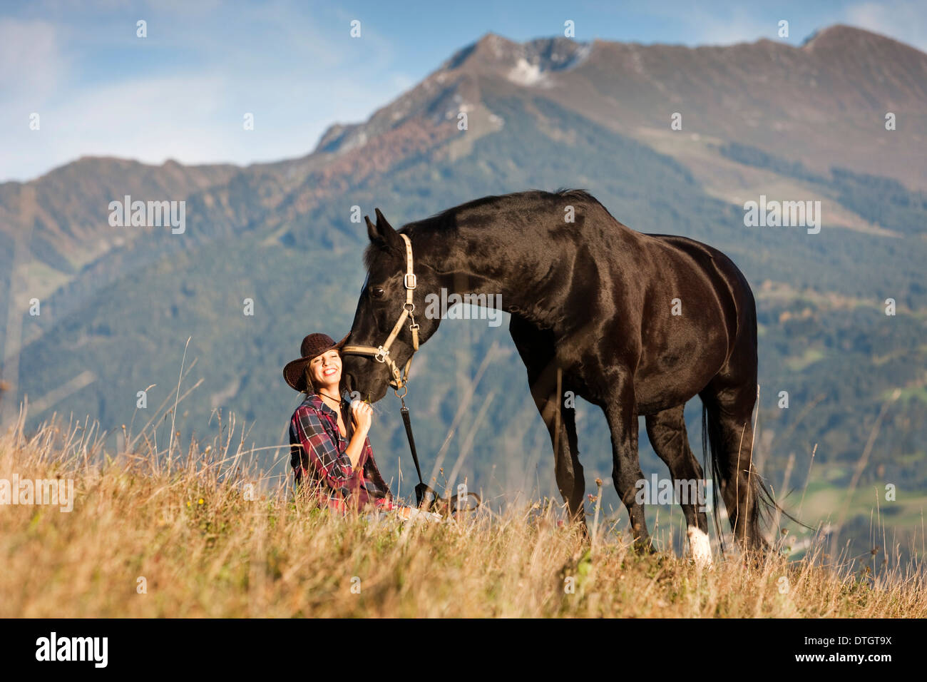 Eine junge Frau mit einem schwarzen Hannoveraner Pferd auf einer Bergwiese im Herbst, Nord-Tirol, Österreich Stockfoto