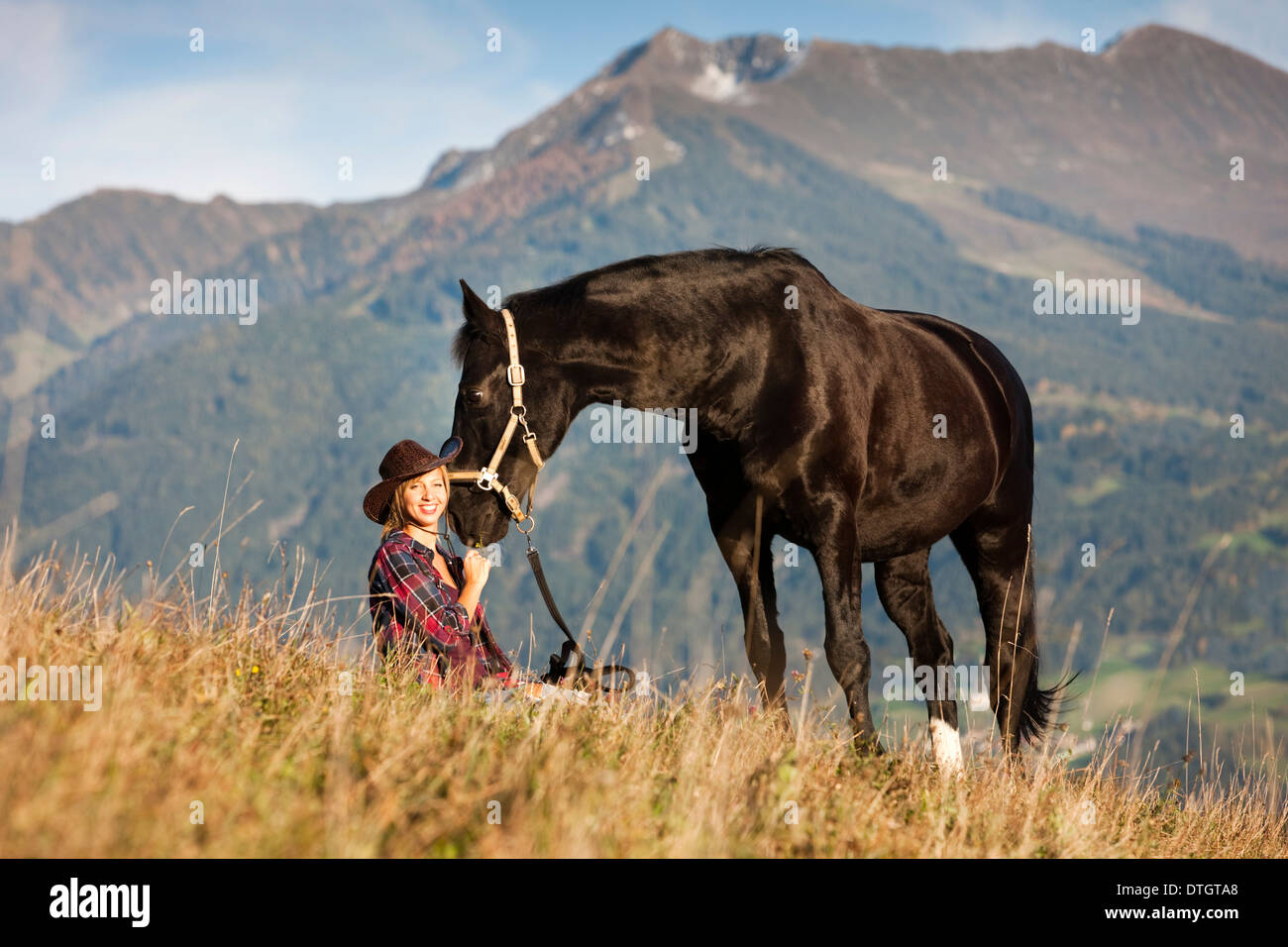 Eine junge Frau mit einem schwarzen Hannoveraner Pferd auf einer Bergwiese im Herbst, Nord-Tirol, Österreich Stockfoto