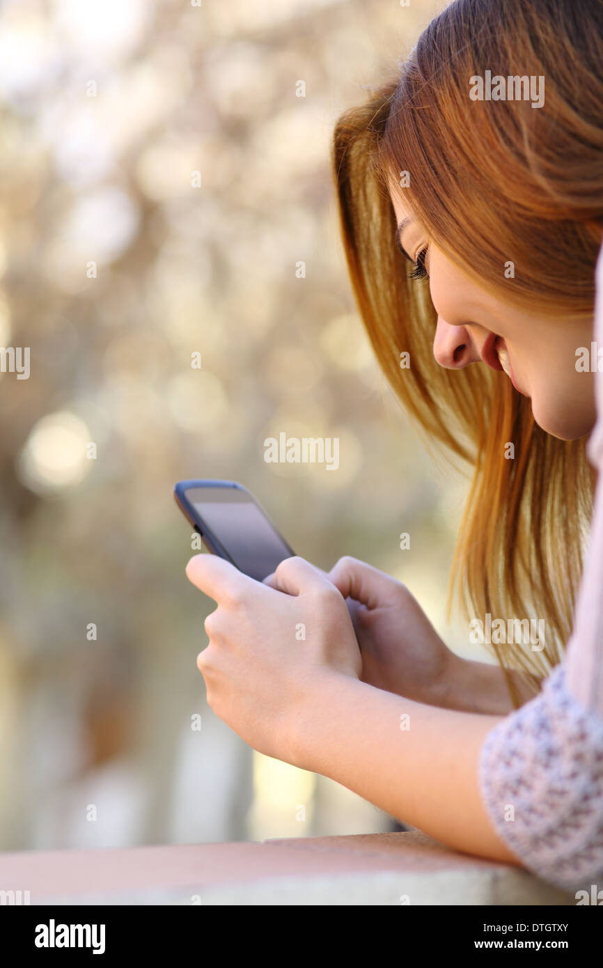 Eine glückliche Frau, die ein Smartphone mit einem Wärme-Hintergrund mit Nahaufnahme Stockfoto