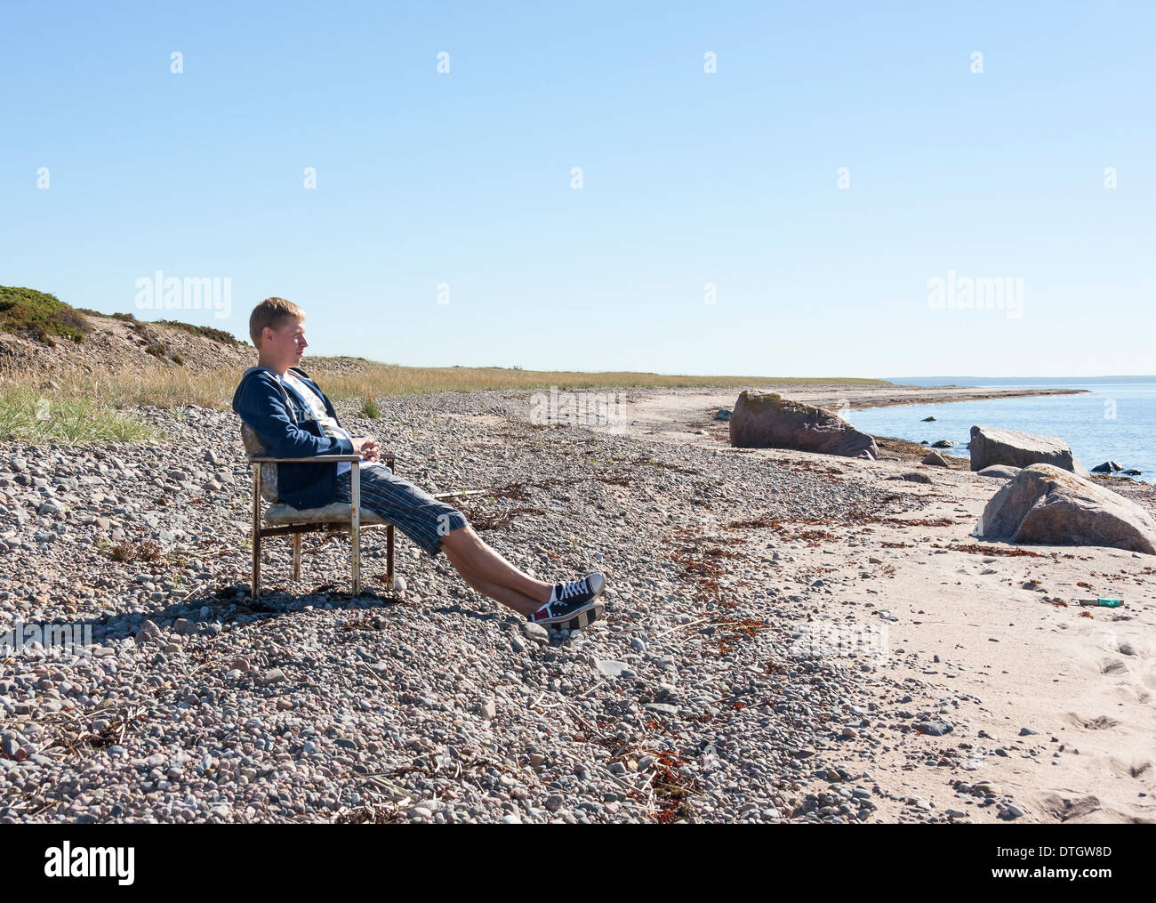 Jungen Erwachsenen Mannes entspannen und sitzen auf Bank in der Nähe von Meer und in Distanz zu beobachten. Stockfoto