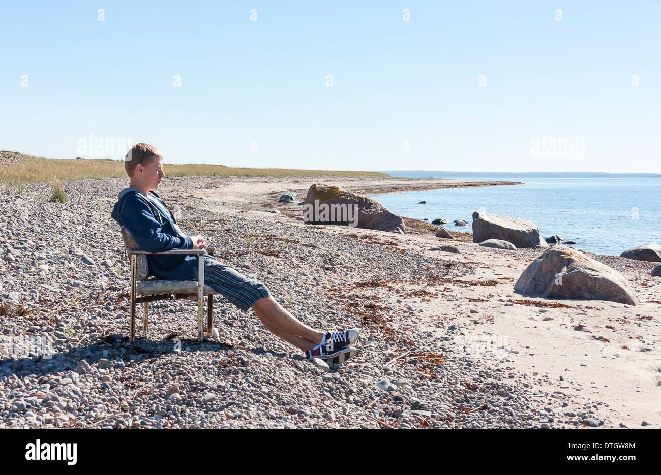 Jungen Erwachsenen Mannes entspannen und sitzen auf Bank in der Nähe von Meer und in Distanz zu beobachten. Stockfoto