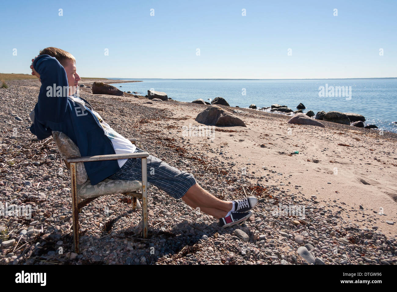 Jungen Erwachsenen Mannes entspannen und sitzen auf Bank in der Nähe von Meer und in Distanz zu beobachten. Stockfoto