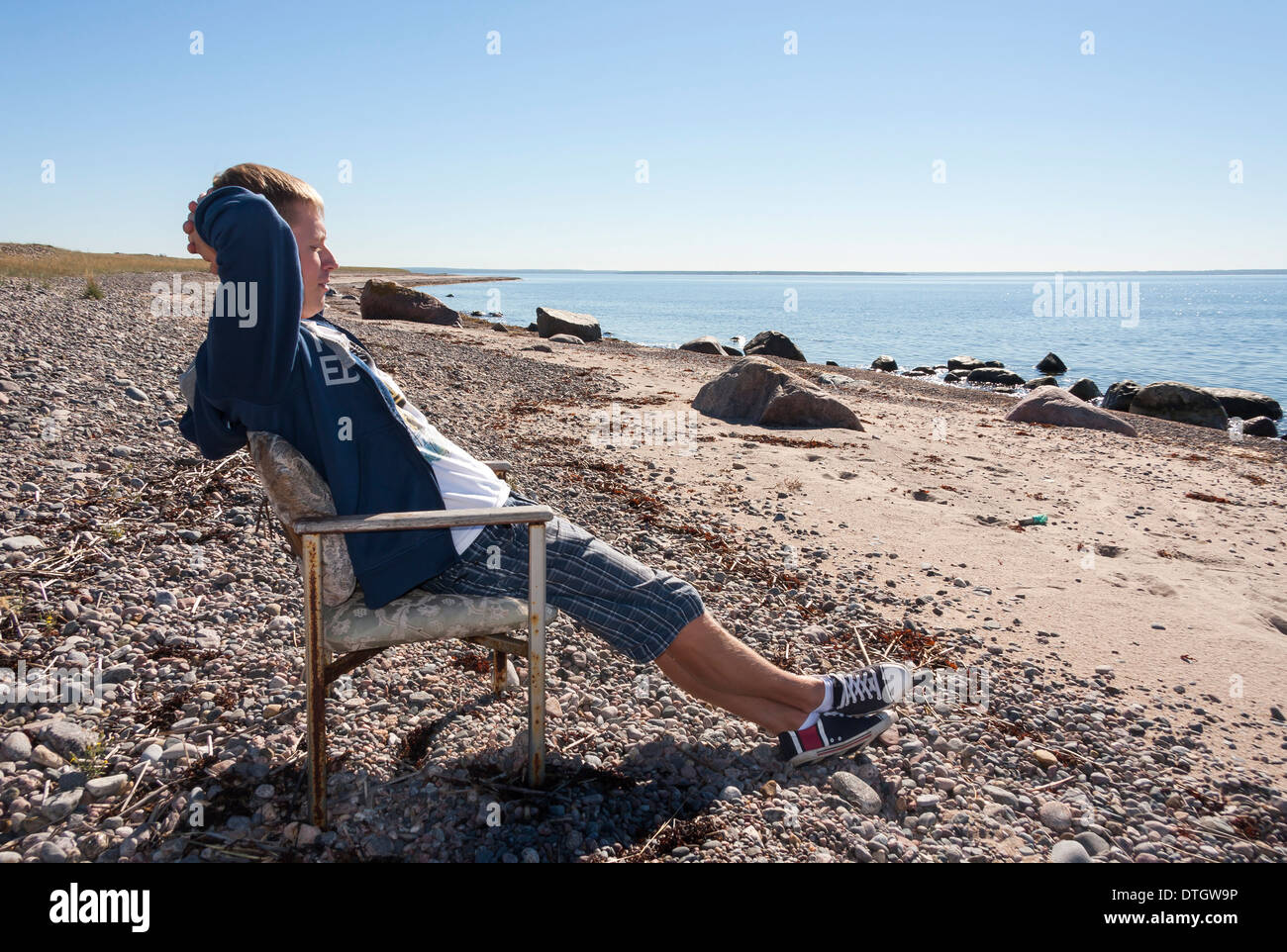Jungen Erwachsenen Mannes entspannen und sitzen auf Bank in der Nähe von Meer und in Distanz zu beobachten. Stockfoto