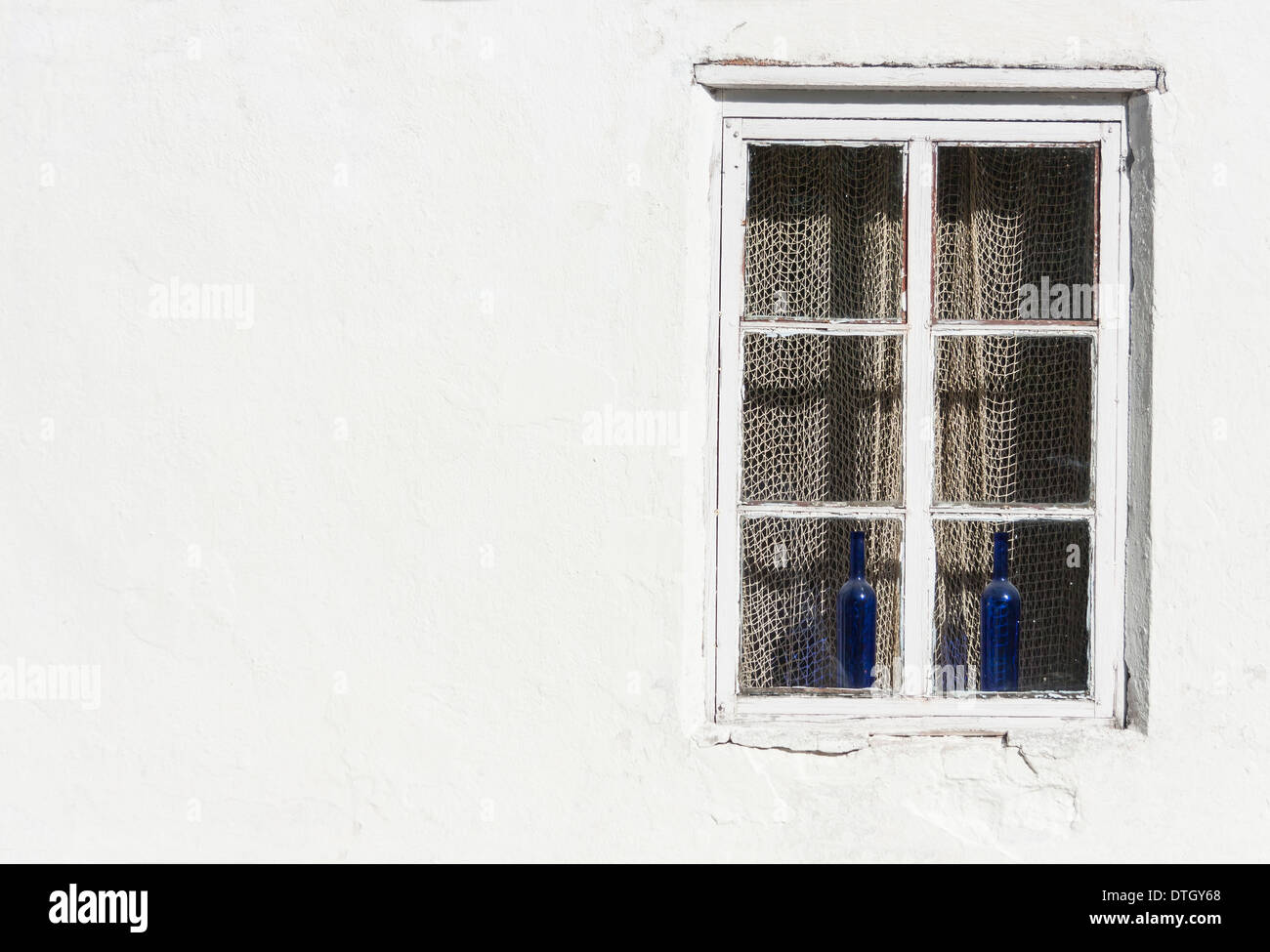 Fenster mit zwei blauen Weinflaschen und Fischernetz in weiße Wand Stockfoto
