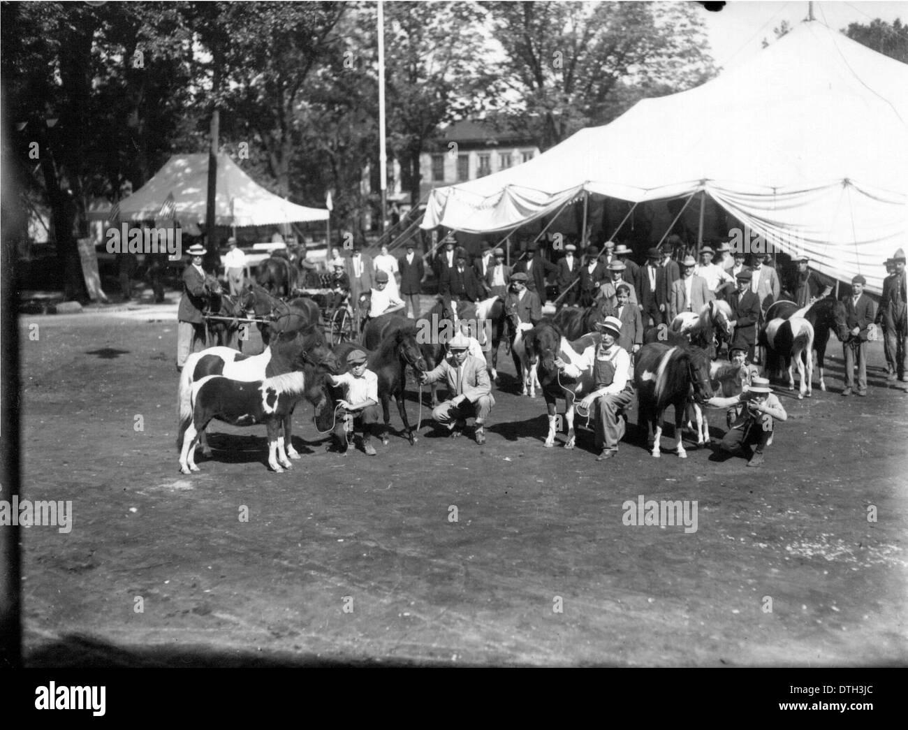 Dieses historische Foto aus der Zeit um 1912 zeigt Männer und Jungen mit Ponys auf der Oxford Street Fair. Das Bild bietet einen Einblick in das Stadtleben von Oxford, Ohio, mit Straßenszenen, die faire Aktivitäten und lokale Pferde zeigen und einen Schnappschuss aus der damaligen Vergangenheit der Gemeinde bieten. Stockfoto
