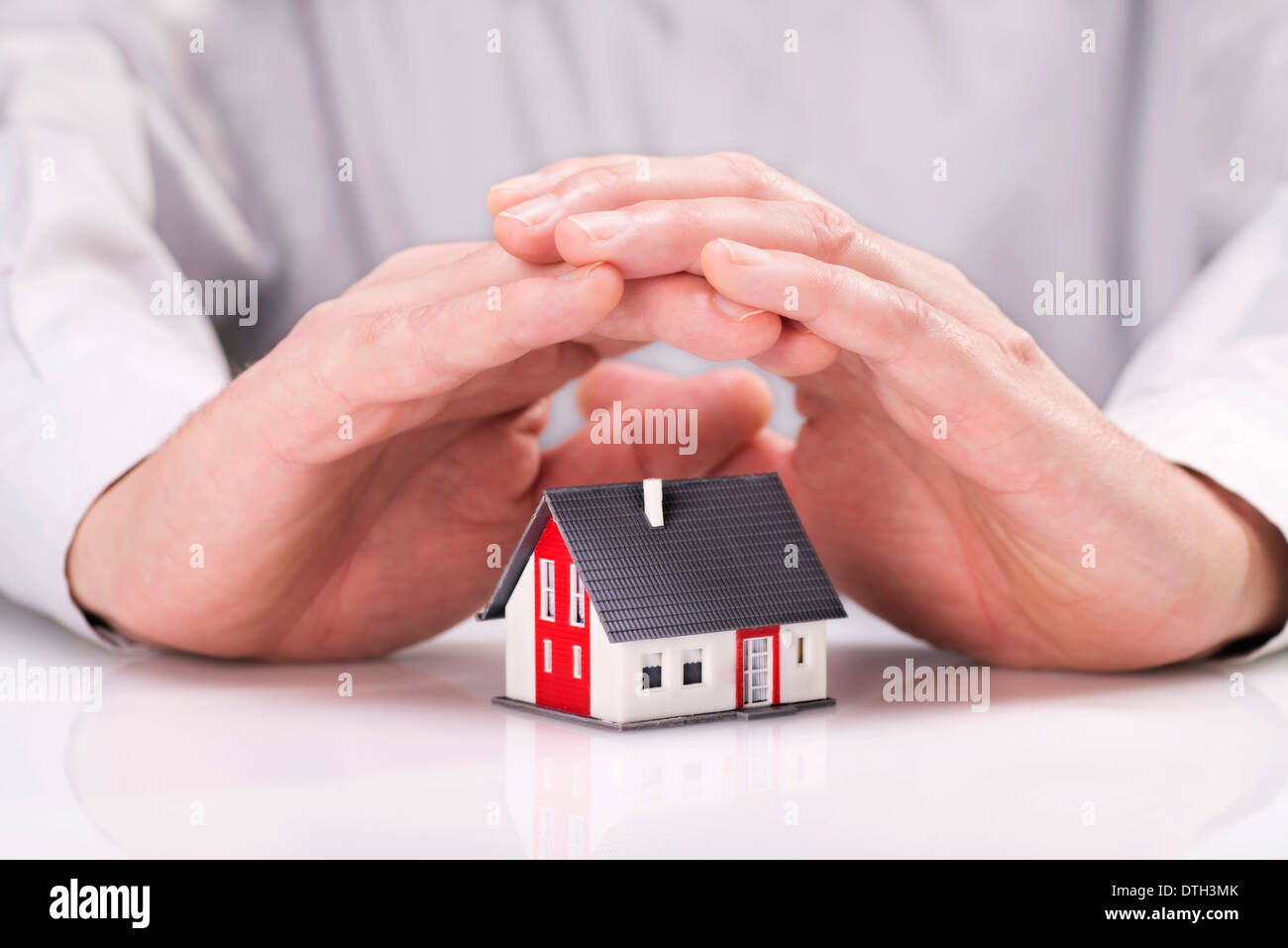 Hände legen sich schützend um ein Haus. Stockfoto