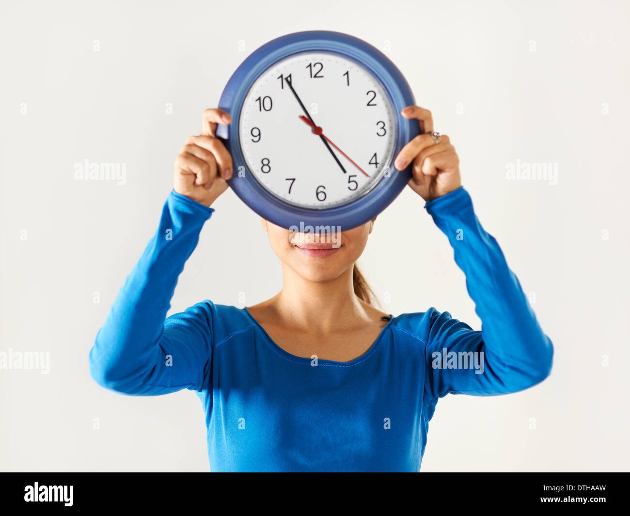 Porträt von asiatischen Geschäftsfrau versteckt sich hinter blauen Uhr und mit Blick auf die Kamera zu Lächeln Stockfoto