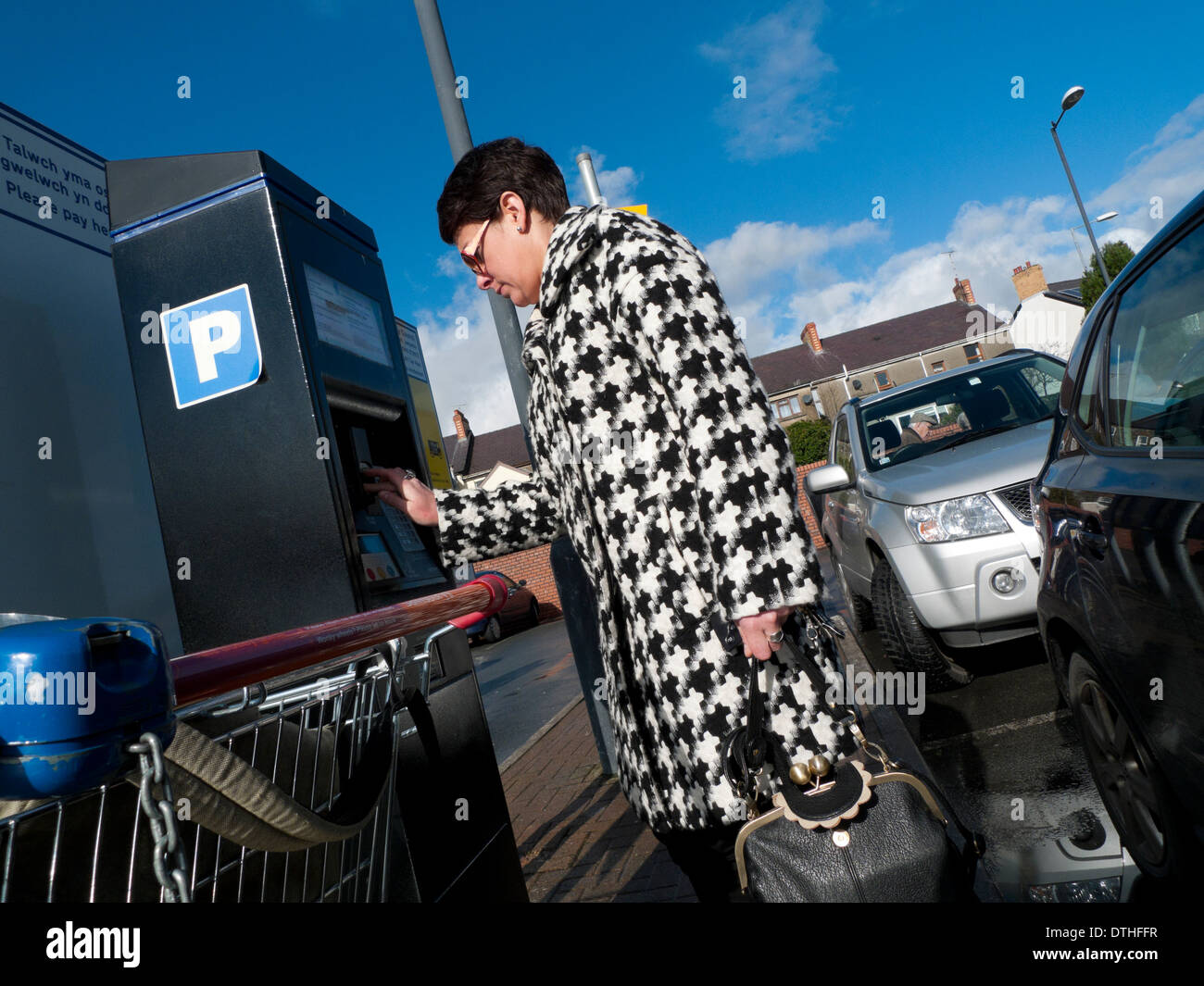 Eine Frau in einem Hahnentritt Muster Stoff Check Mantel, Geld in einen Automaten in einem Supermarkt-Parkplatz UK KATHY DEWITT Stockfoto