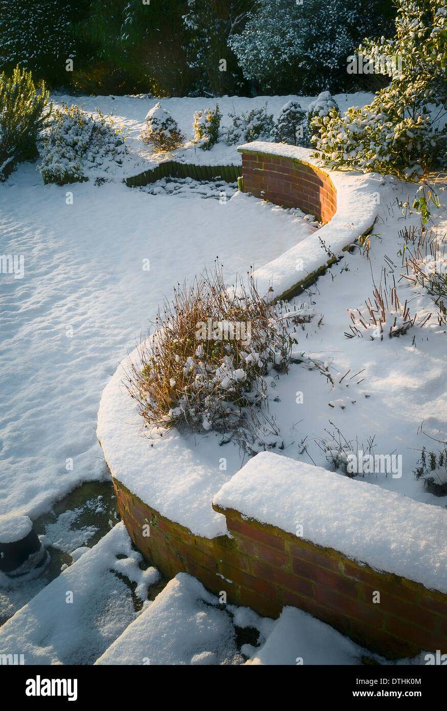 Winter in einem englischen Garten mit geschwungenen Stützmauer und Schritte auf Rasen UK Stockfoto