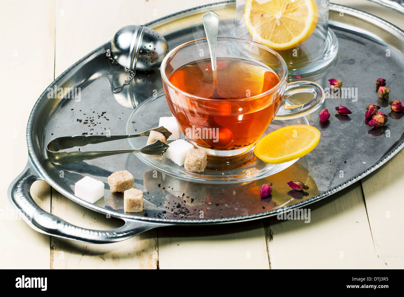 Glastasse Tee mit Würfelzucker, Zitrone und trockenen Rosenknospen, serviert auf Silber Vintage Tablett auf weißer Holztisch. Stockfoto