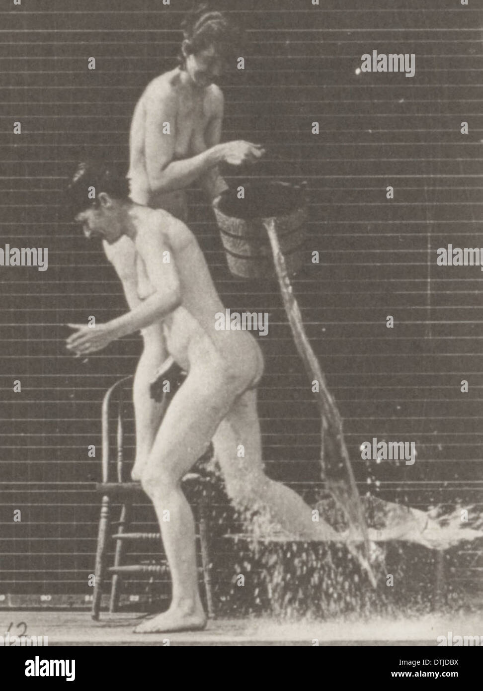 Ein Vintage-Foto einer nackten Frau, die Wasser aus einem Eimer über eine andere nackte Frau gießt, wobei der Schwerpunkt auf menschliche Interaktion und die natürliche Umgebung gelegt wird. Stockfoto