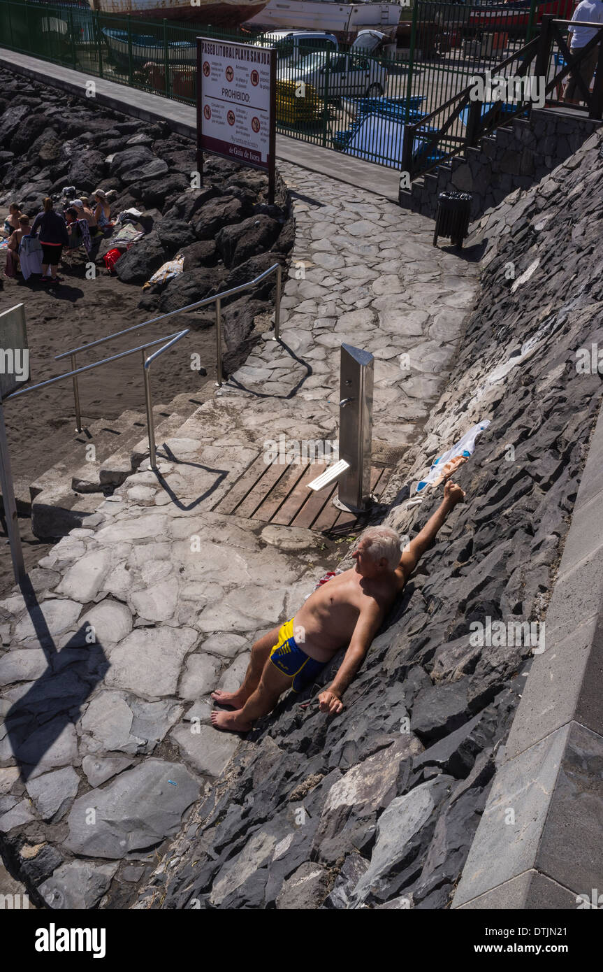 Mann zum Sonnenbaden Stand gegen vulkanischen Steinmauer in Playa San Juan Strand, Teneriffa, Kanarische Inseln, Spanien Stockfoto