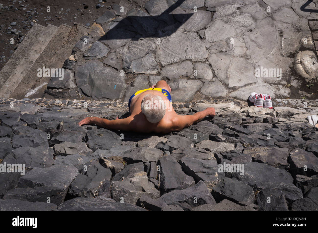 Mann zum Sonnenbaden Stand gegen vulkanischen Steinmauer in Playa San Juan Strand, Teneriffa, Kanarische Inseln, Spanien Stockfoto
