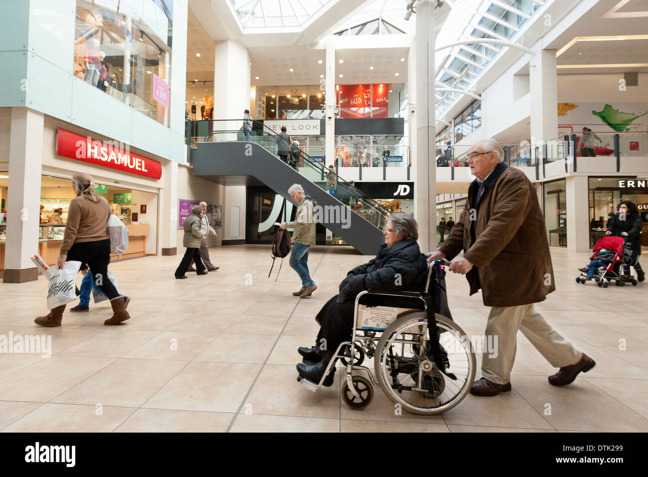Behindertengerechter Zugang zu den Geschäften - ein älteres Ehepaar mit einer behinderten Person in einem Rollstuhl in einer Shopping Mall, England UK Stockfoto