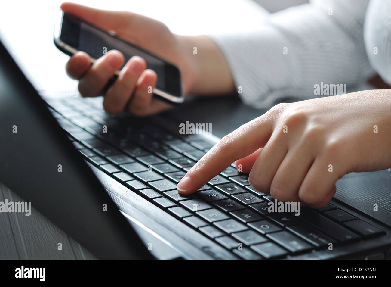 Weibliche Hände mit Laptop-Tastatur und hält Mobiltelefon Stockfoto