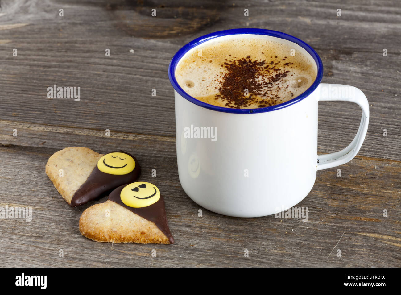 Emaille Becher mit heißem Kaffee und zwei Kekse mit Herzform auf alten rustikalen Holzbrett mit und textfreiraum linken Bildbereich Stockfoto