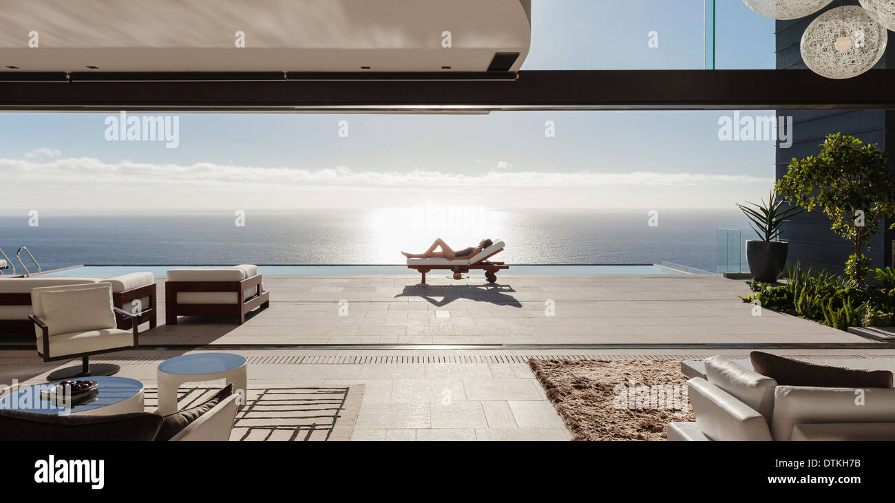 Frau Sonnenbaden auf Liegestuhl am Pool mit Blick auf Meer Stockfoto