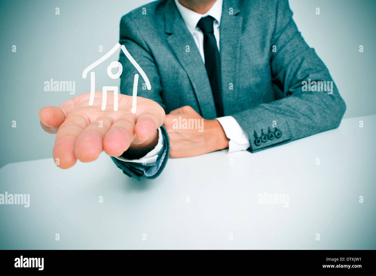 ein Geschäftsmann in einem Schreibtisch zeigt eine Zeichnung eines Hauses in der Hand sitzen Stockfoto