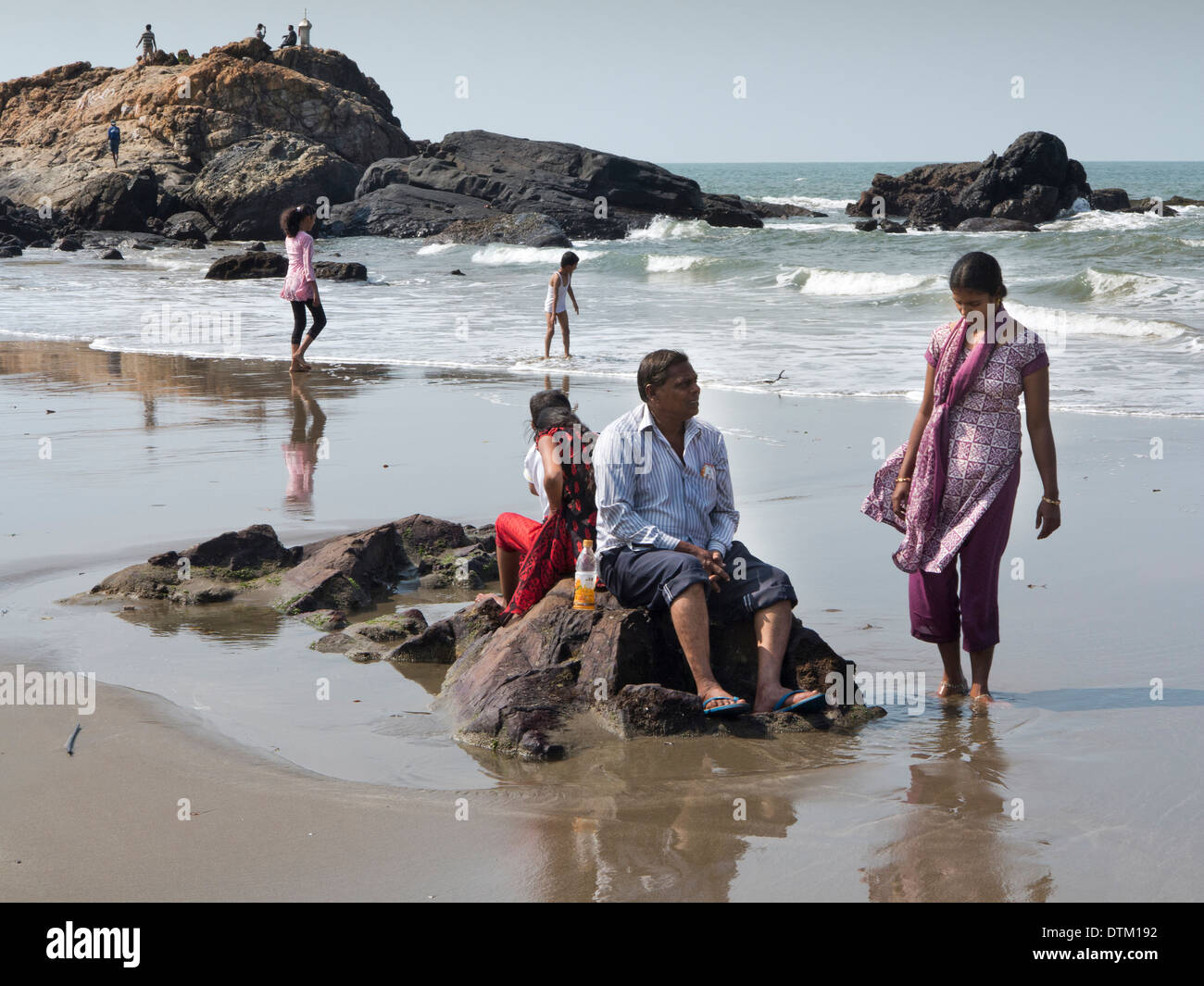 Indien, Goa, Vagator Strand, indische Touristen Sittng auf Felsen am Meeresufer Stockfoto