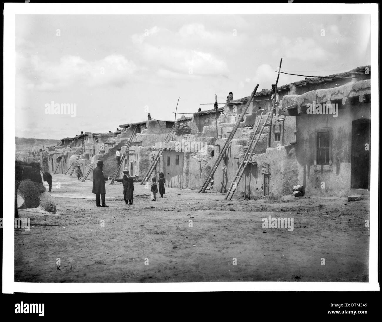 Ein Straßenblick auf Acoma Pueblo im Jahr 1886, mit traditionellen lehmziegelwohnungen und einem Einblick in das tägliche Leben in der indianischen Gemeinde. Das Bild spiegelt den architektonischen Stil und die Kultur der Zeit wider. Stockfoto