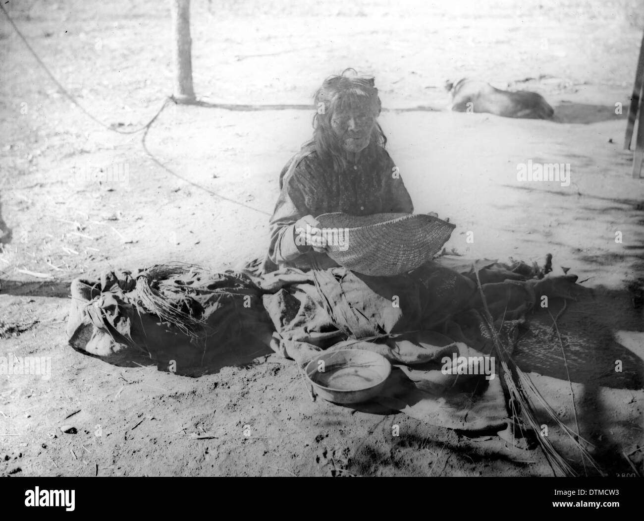Eine Yokut-Indianerin sieht Maismehl in einem Schilfkorb, der um 1900 in der Nähe von Porterville, Kalifornien, entnommen wurde und das indigene Leben darstellt. Stockfoto