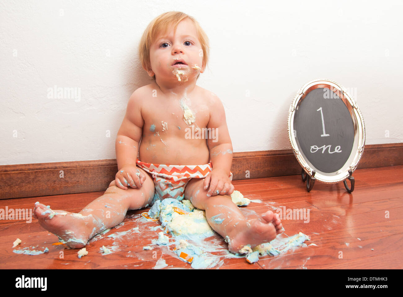 Baby Boy schaltet man mit einem smash Kuchen und orange Chevron Windeln Hartholz-Fußboden Stockfoto