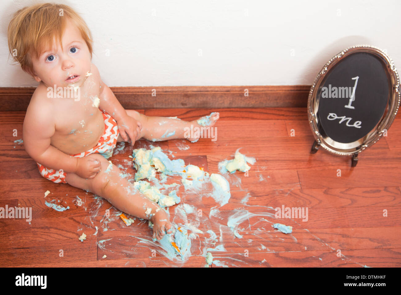 Baby Boy schaltet man mit einem smash Kuchen und orange Chevron Windeln Hartholz-Fußboden Stockfoto