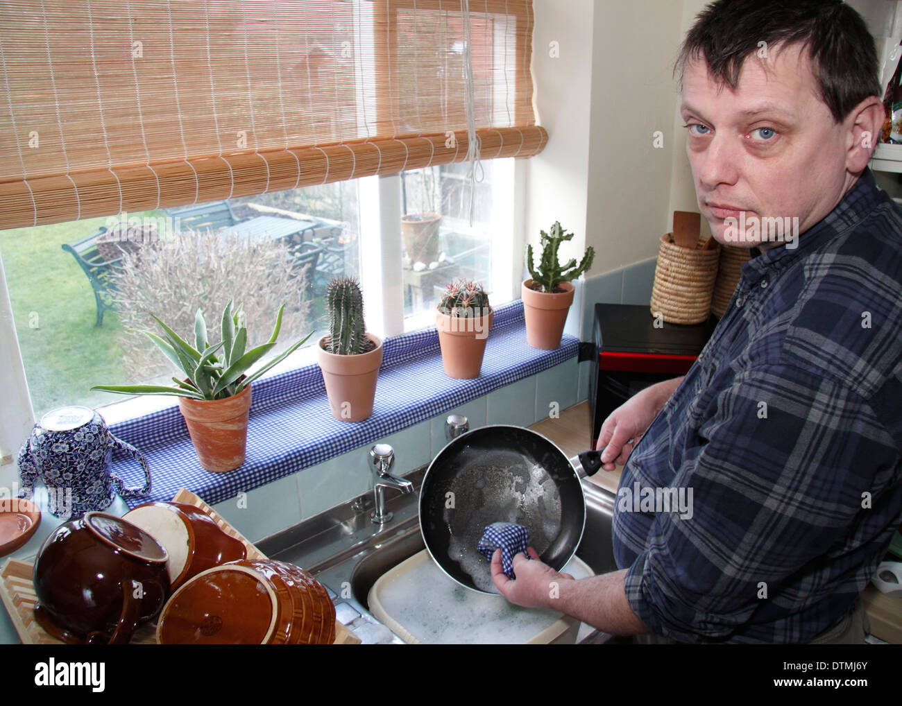 Mann waschen Töpfe mit kleinen Enthuiasm bei einer Küchenspüle zu Hause, England, UK Stockfoto