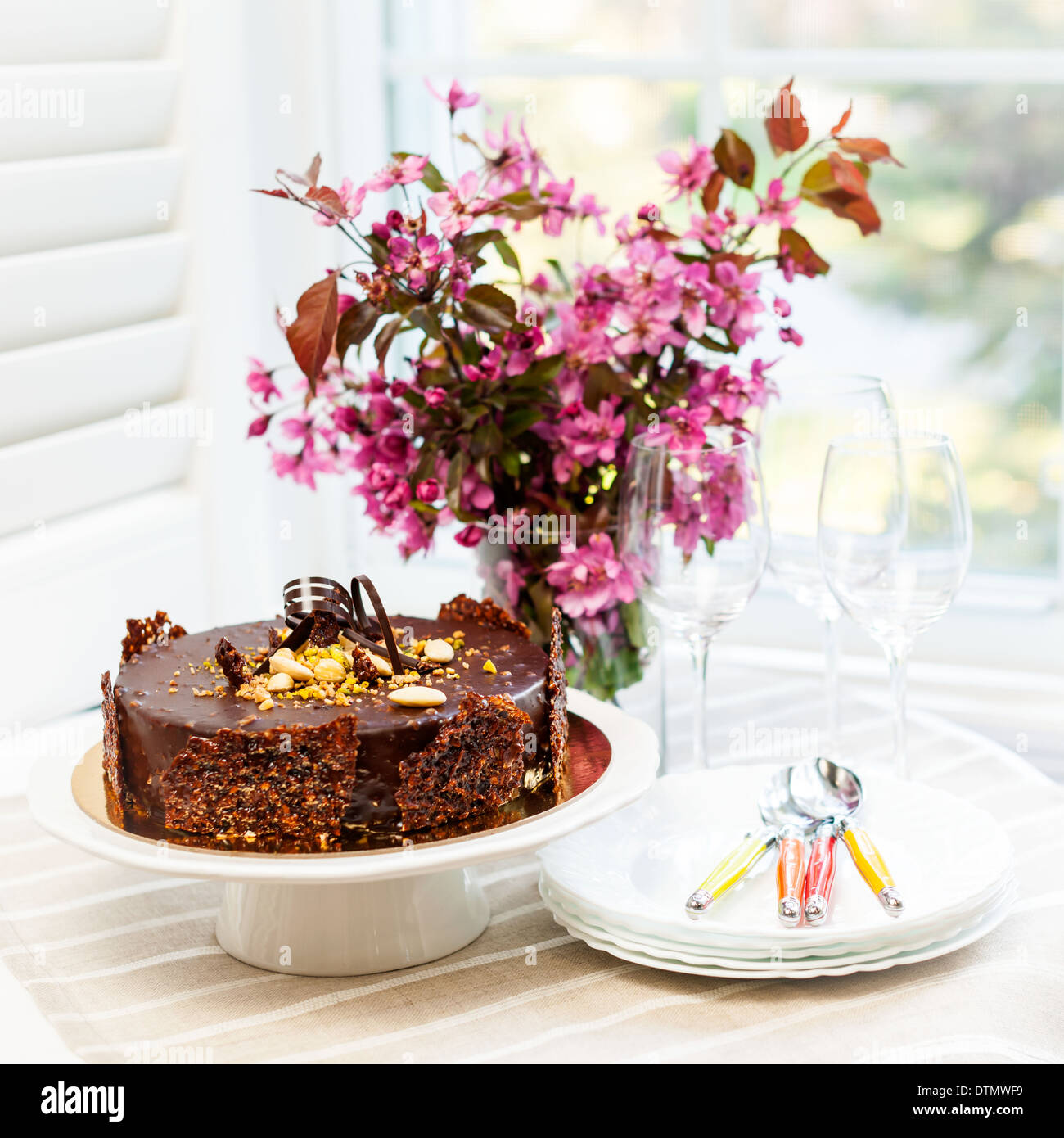 Runde Gourmet-Schokolade Kuchen auf den Tisch neben Fenster mit Tellern, Besteck und rosa Frühlingsstrauß Stockfoto