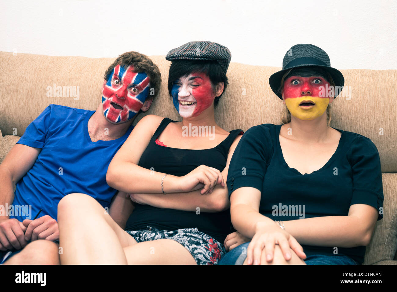 Gruppe von lustigen Menschen mit bemalten Fahnen auf ihren Gesichtern und sitzt auf dem Sofa. Stockfoto