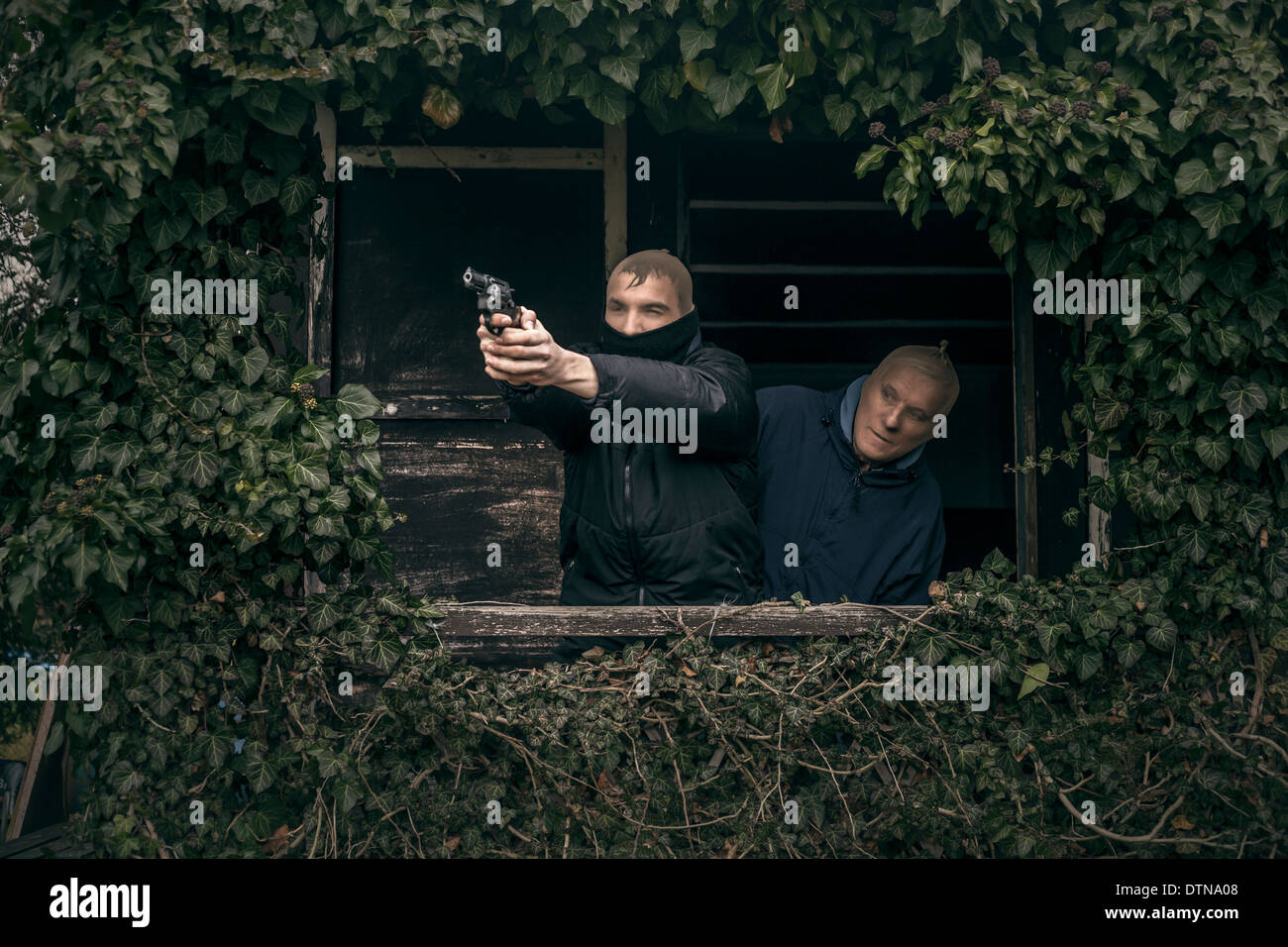 Zwei maskierte bewaffnete Männer verstecken auf bewachsenen Veranda der alten Kabine. Stockfoto